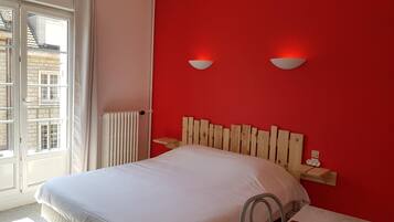 Une chambre avec un mur rouge, un lit blanc, une tête de lit en bois et deux appliques murales.