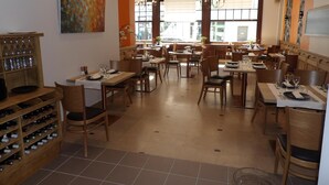 A restaurant with multiple dining tables and chairs, a wine rack, and a painting on the wall.