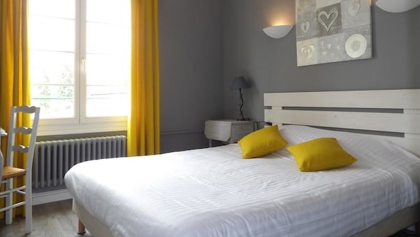 A bedroom with a bed, yellow pillows, a nightstand, a lamp, and a window with yellow curtains.