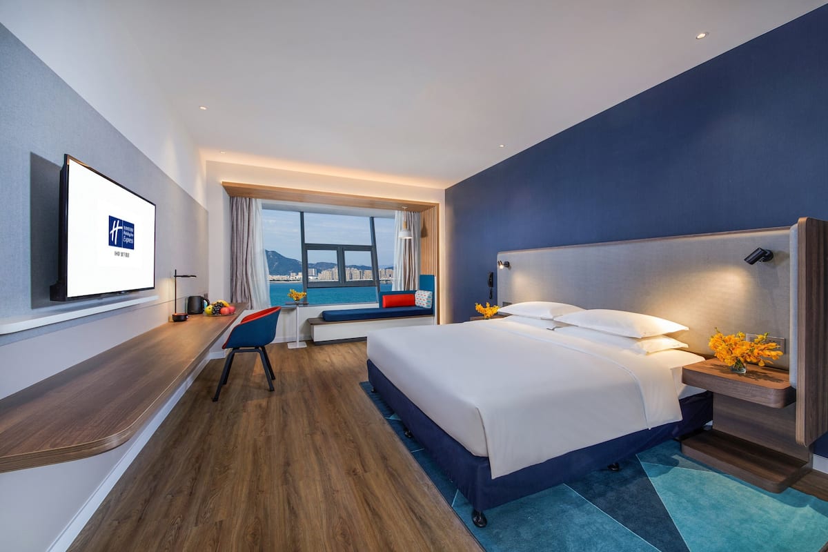 A modern hotel room with a large bed, a desk, and a view of the city.