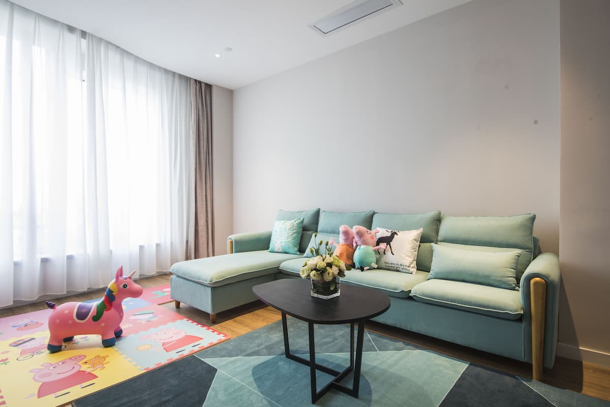 A living room with a teal sofa, a black coffee table, and a colorful play mat.
