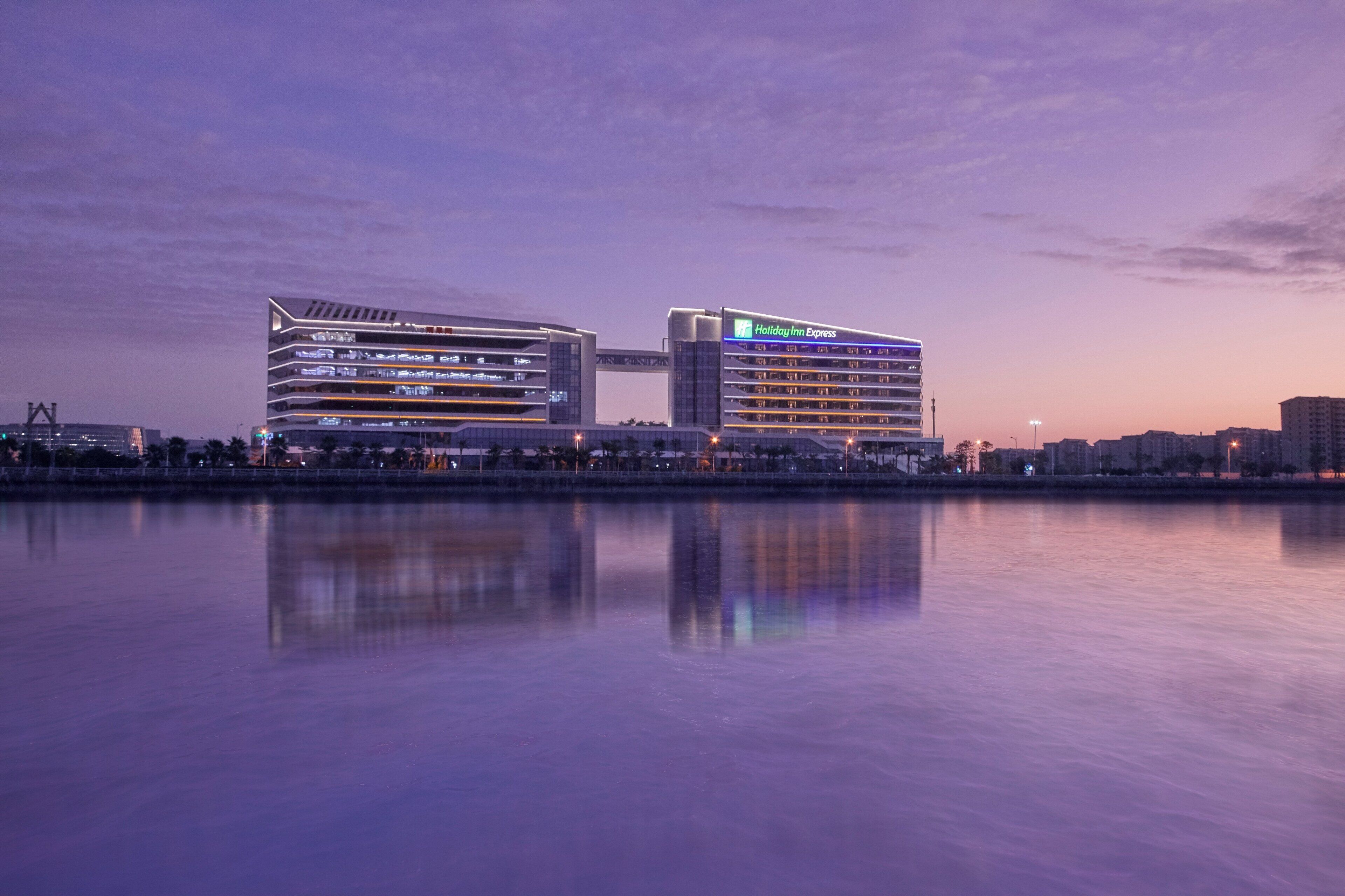 A modern hotel with multiple floors and balconies, situated by a body of water.