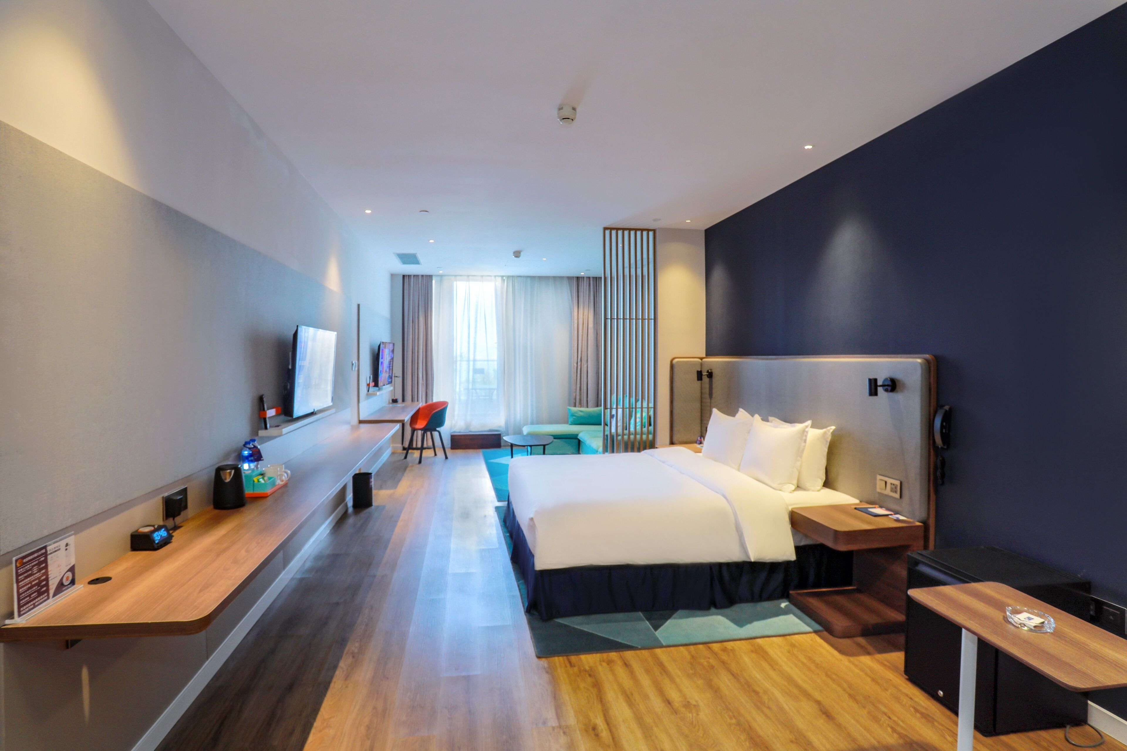 A modern hotel room with a large bed, a desk, a chair, a small table, and a TV.