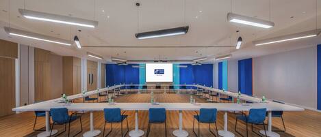 A conference room with a long table, blue chairs, and a presentation screen.