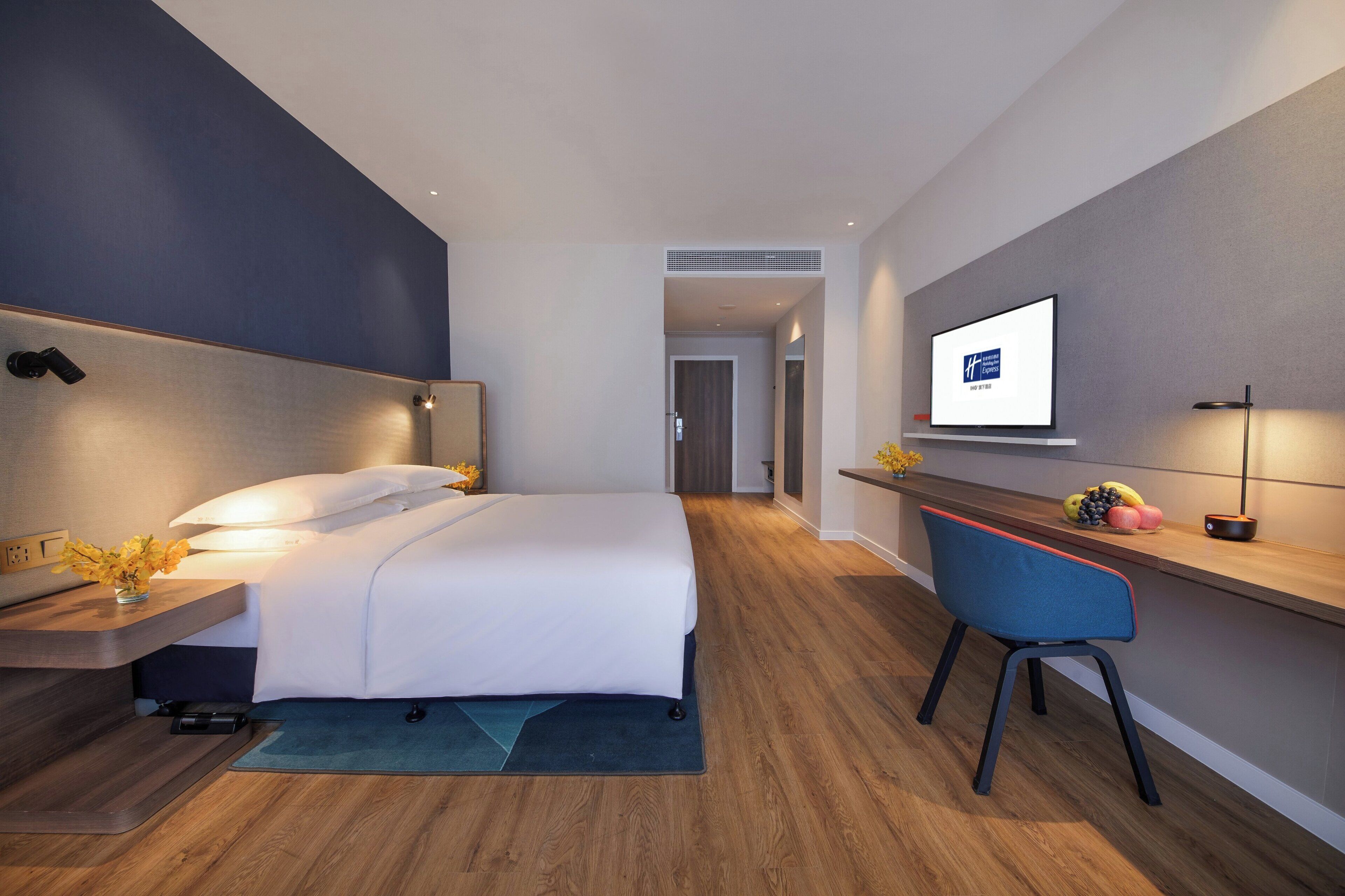 Una habitación de hotel moderna con cama, mesita de noche, lámpara, televisión y escritorio con silla.