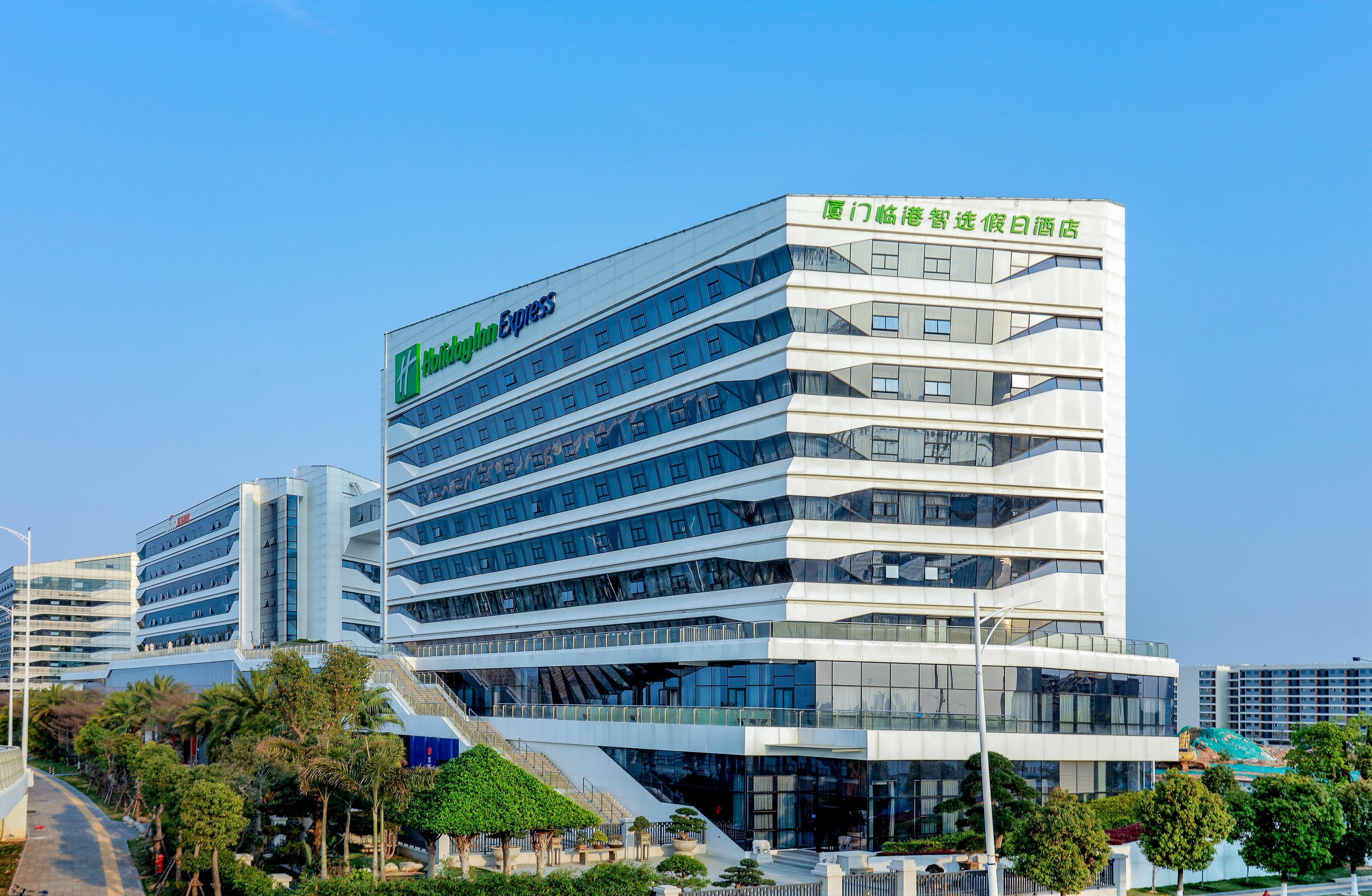 Un hotel moderno con un llamativo letrero de 'Holiday Inn Express', varios pisos y una escalera que conduce a la entrada.