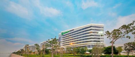 A modern hotel building with a prominent sign, surrounded by a landscaped area with benches and trees.
