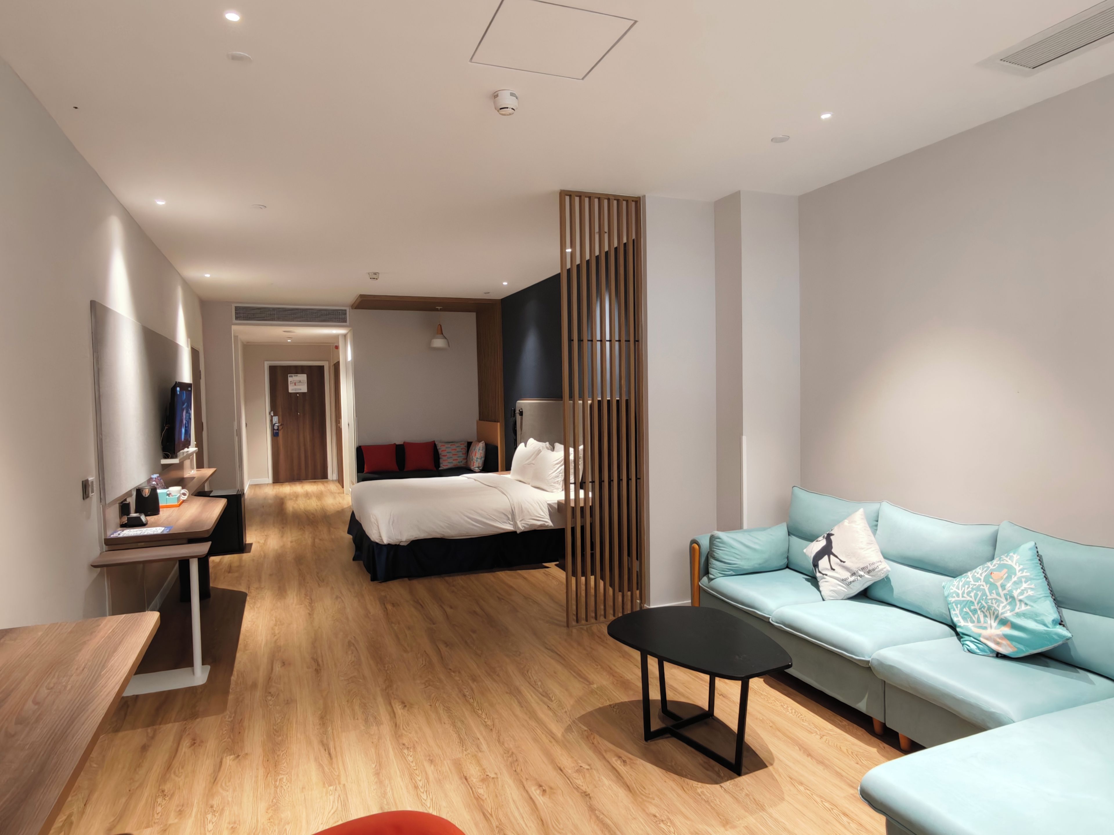 Una camera d'albergo moderna con pavimento in legno, un letto con biancheria bianca, un divano blu, un piccolo tavolo nero e una TV su un mobile.
