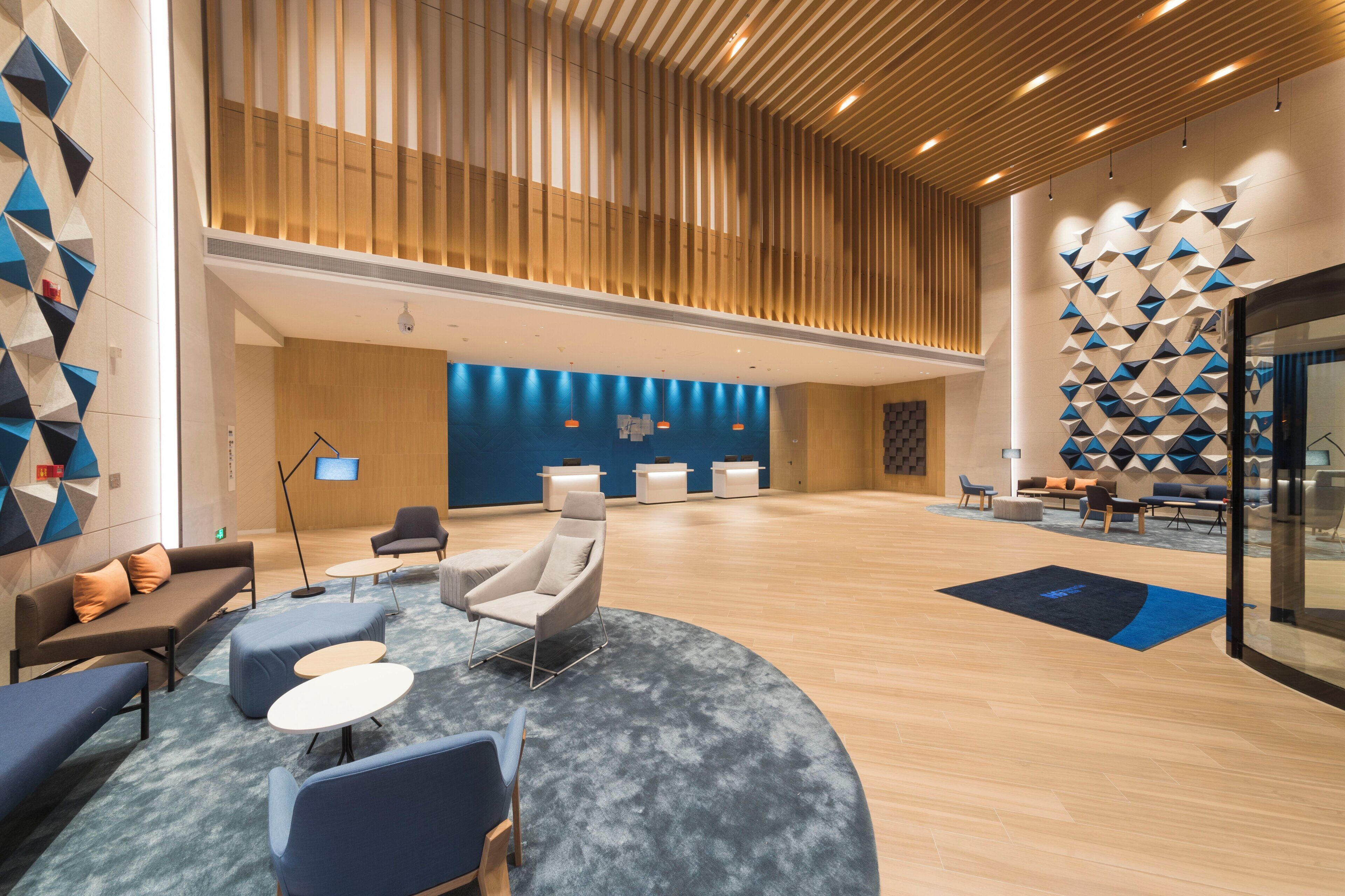 A spacious lobby with a modern design, featuring a reception desk, seating area with sofas and chairs, and a decorative wall with geometric patterns.