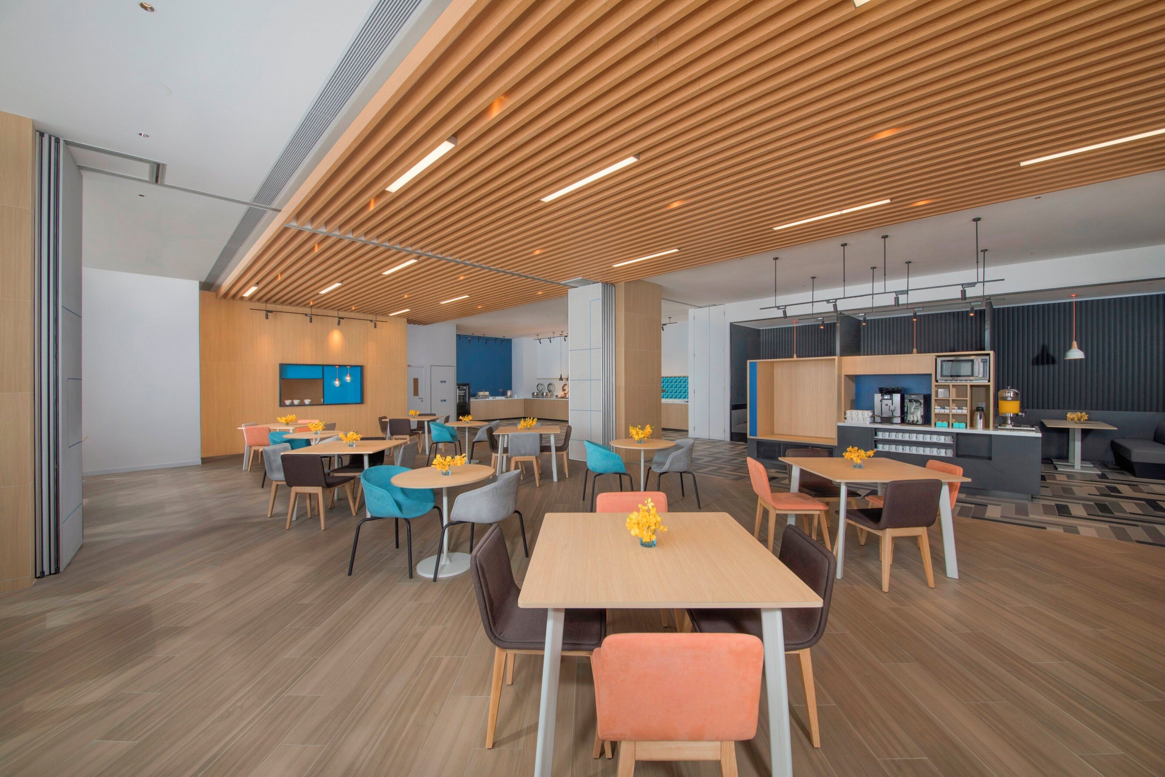 A modern interior with wooden slatted ceilings, multiple seating areas with tables and chairs, and a kitchenette area.