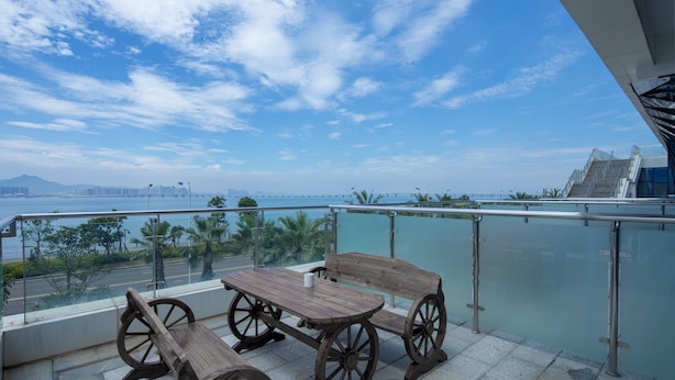 A balcony with a wooden table and chairs, offering a view of the sea and a bridge in the distance.