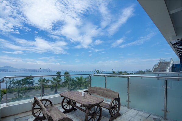 A balcony with a wooden table and chairs, offering a view of the sea and a bridge in the distance. - Holiday Inn Express Xiamen Airport Zone by IHG (Xiamen)