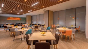 A modern dining area with wooden ceiling panels, orange pendant lights, and tables with chairs.