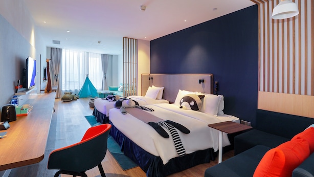 Une chambre d’hôtel moderne avec un grand lit, un bureau avec une chaise, un canapé et une tente en arrière-plan.