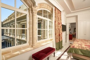 A hotel room with large windows, a bed, a bench, and a view of an outdoor terrace. - Hotel Casa Palacio María Luisa 5* GL by Kaizen Hoteles (Jerez de la Frontera)