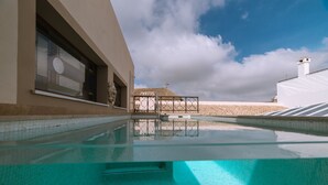 A swimming pool with clear water, a tiled deck, and a building with large windows and a tiled roof in the background.