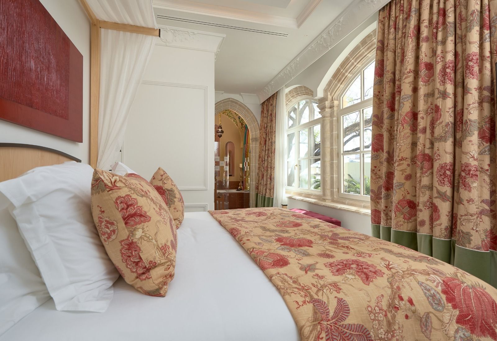 A hotel room with a large bed, floral-patterned bedspread, and curtains.