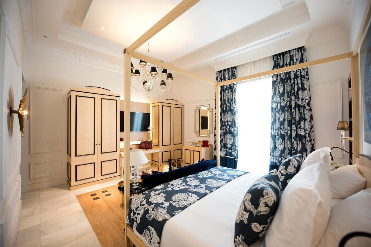 A hotel room with a large bed, a wardrobe, a vanity with a mirror, and a chandelier.