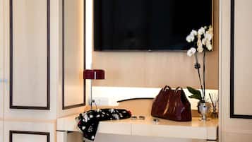 Et moderne værelse med et stort fladskærms-tv på væggen, et skrivebord med lampe, en håndtaske og en orkidé i potte.