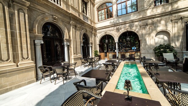 An outdoor patio with a pool, tables, and chairs.