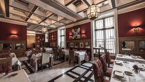 A formal dining area with tables set for service, large windows, and a high ceiling with intricate moldings.
