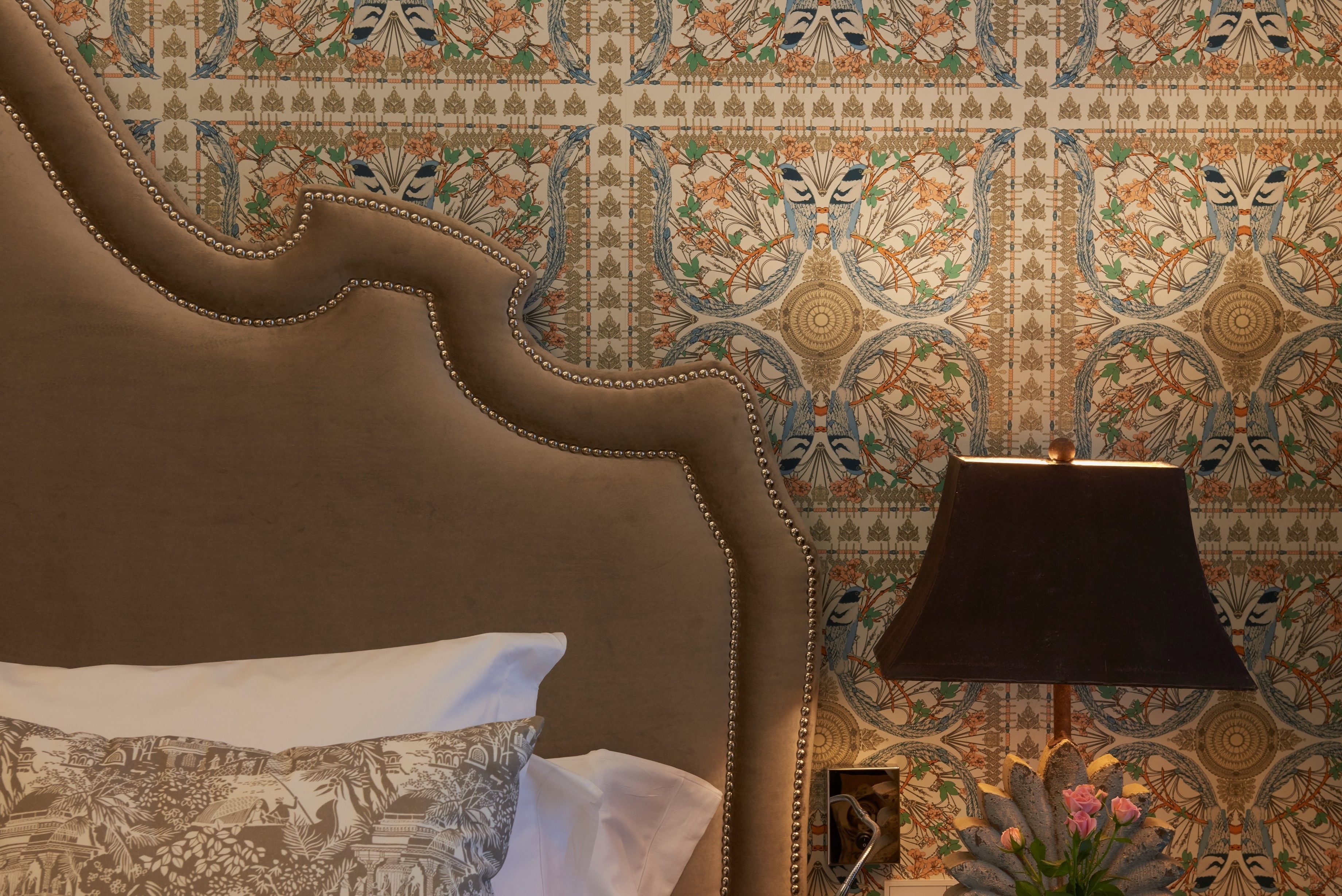 Un letto con una testiera decorata, una lampada e un'asse da notte con un'idea floreale.