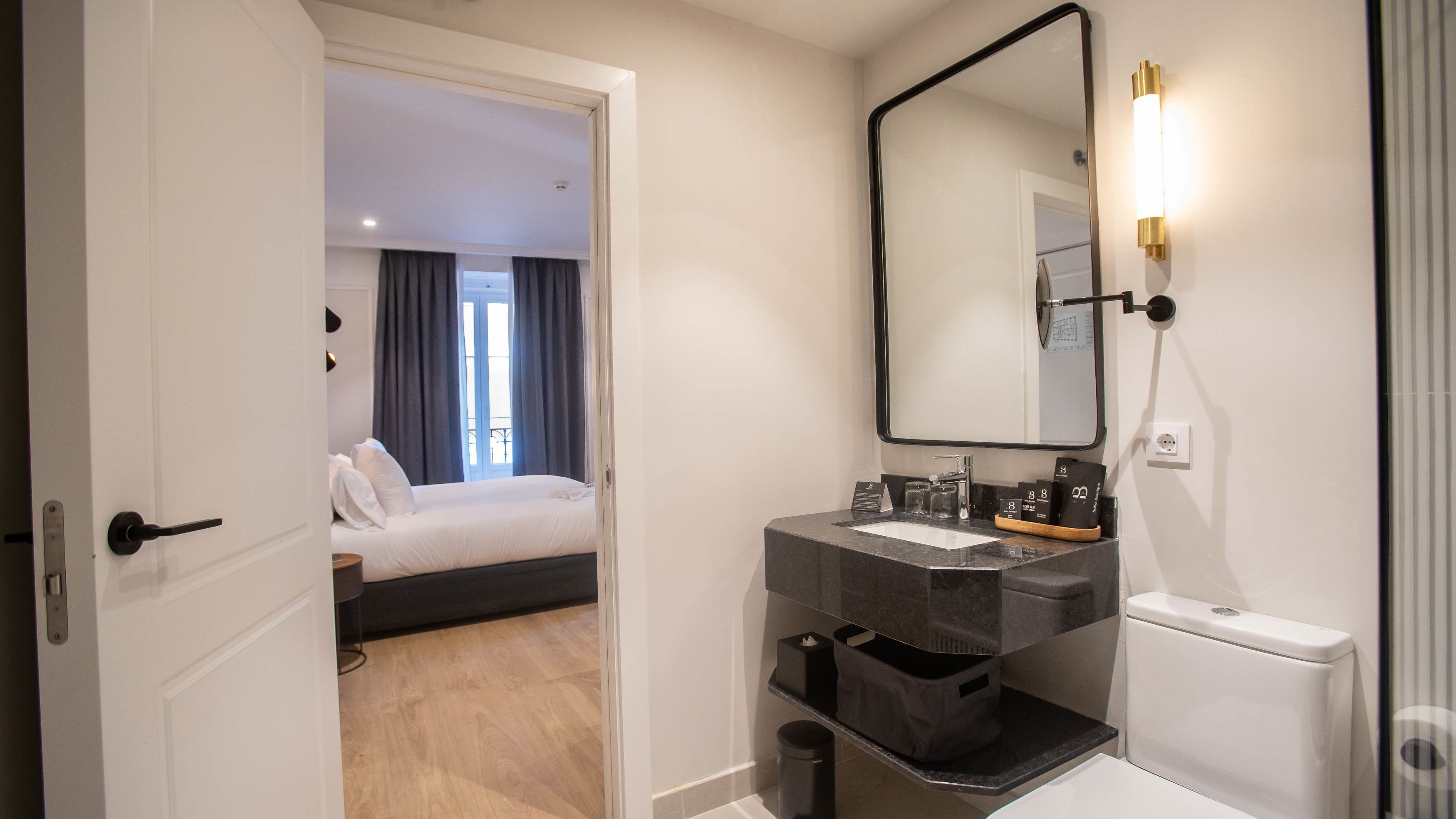 A hotel room with a bed, a bathroom with a sink, mirror, and toiletries.