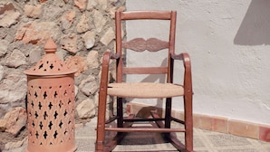 A rustic outdoor seating area with a wooden chair and a terracotta lantern against a stone wall and a white wall. - La Casa de Bobadilla Alojamiento Rural (Alcaudete)