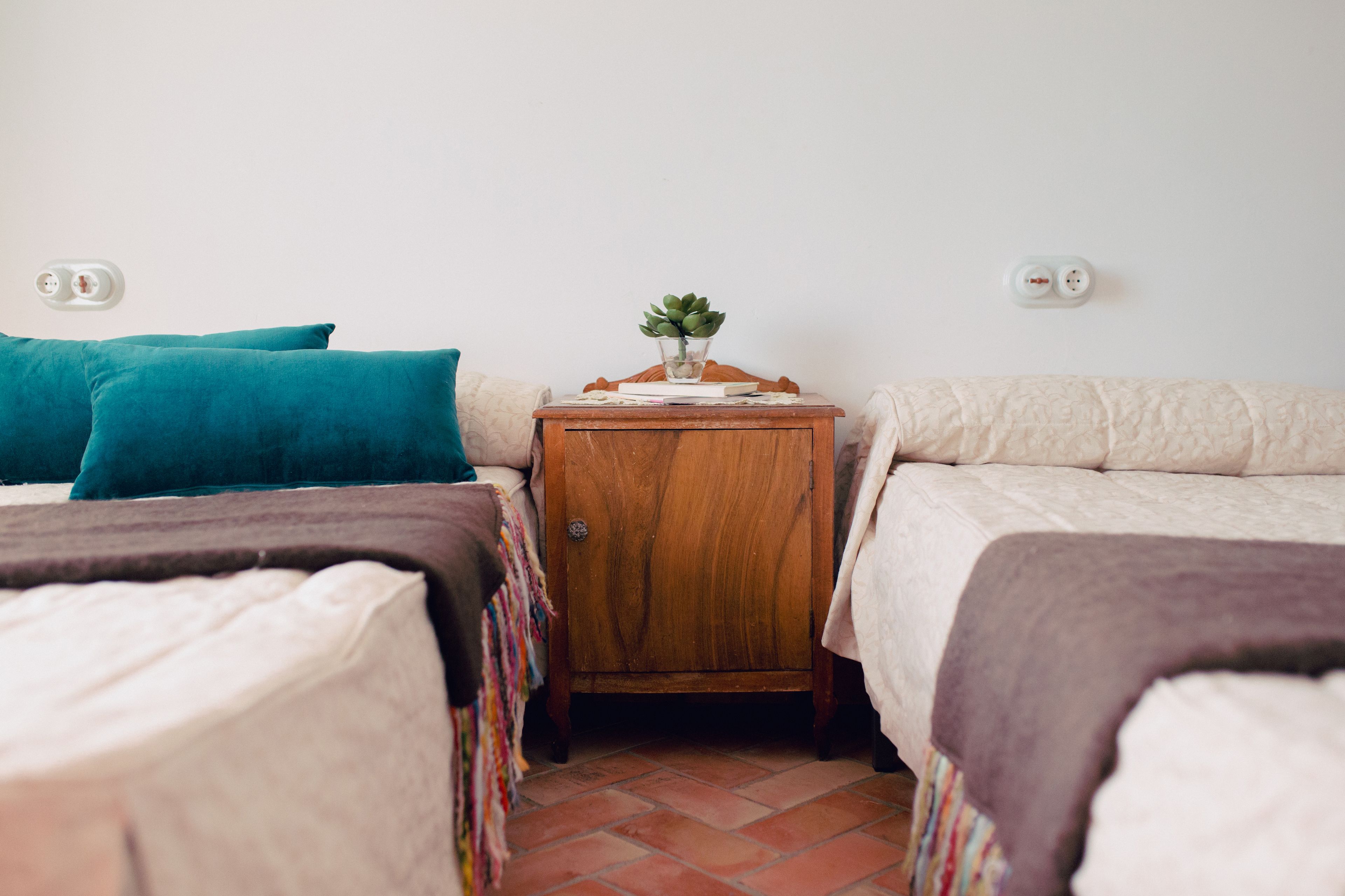 Ein Zimmer mit zwei Betten, einem kleinen Nachttisch mit Pflanze und einem Fliesenboden.