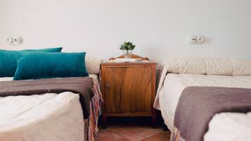Ein Zimmer mit zwei Betten, einem kleinen Nachttisch mit Pflanze und einem Fliesenboden.