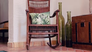 A wooden rocking chair with a patterned cushion, a green bottle, and a brown suitcase by a tiled floor. - La Casa de Bobadilla Alojamiento Rural (Alcaudete)