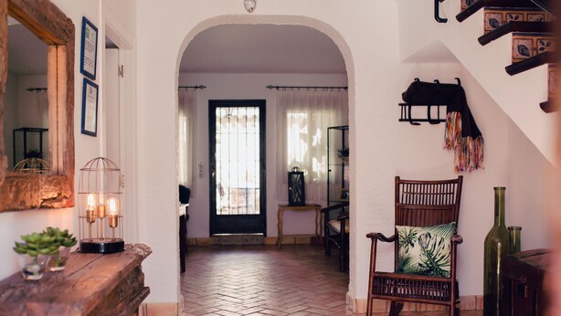 A hallway with a wooden bench, a chair with a cushion, a mirror, and a door leading to another room. - La Casa de Bobadilla Alojamiento Rural (Alcaudete)