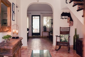A hallway with a wooden bench, a chair with a cushion, a mirror, and a door leading to another room. - La Casa de Bobadilla Alojamiento Rural (Alcaudete)