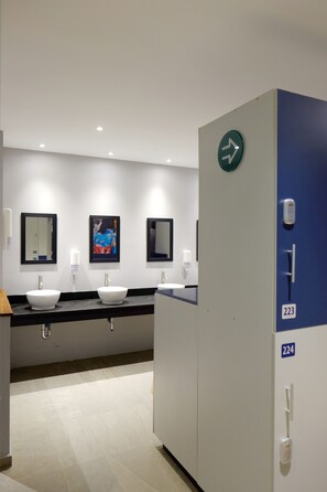 Un baño moderno con tres lavamanos, espejos y una señalización.
