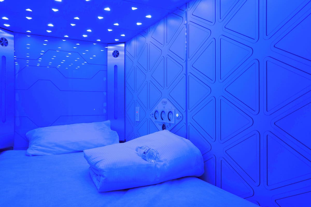 Een kamer met een geometrisch wandontwerp, een bed met witte beddengoed en een bedieningspaneel aan de muur.