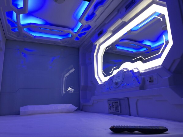 Una habitación futurista con una cama, un panel de control y una ventana con iluminación azul.
