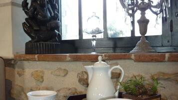 A table with a tea set, a bowl of cookies, and a window with a decorative statue.