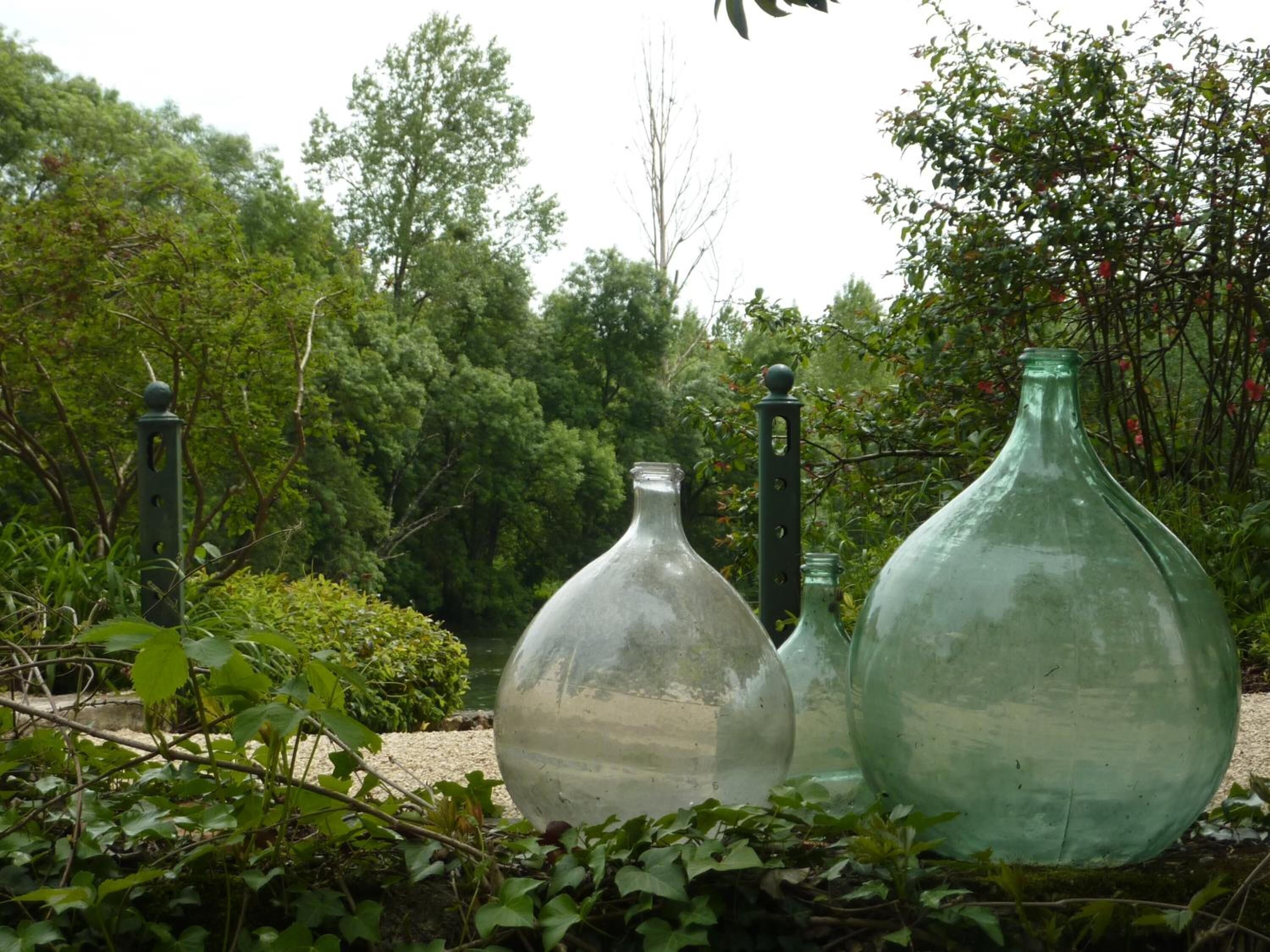 Three glass bottles in a garden setting with greenery and trees in the background.