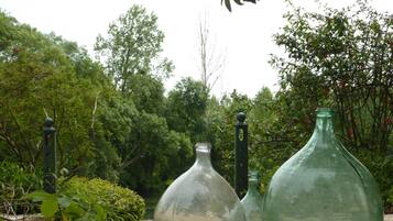 Three glass bottles in a garden setting with greenery and trees in the background.