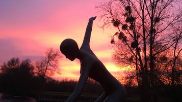 Una statua raffigura una persona in posa dinamica, con un corpo d'acqua e un tramonto sullo sfondo.