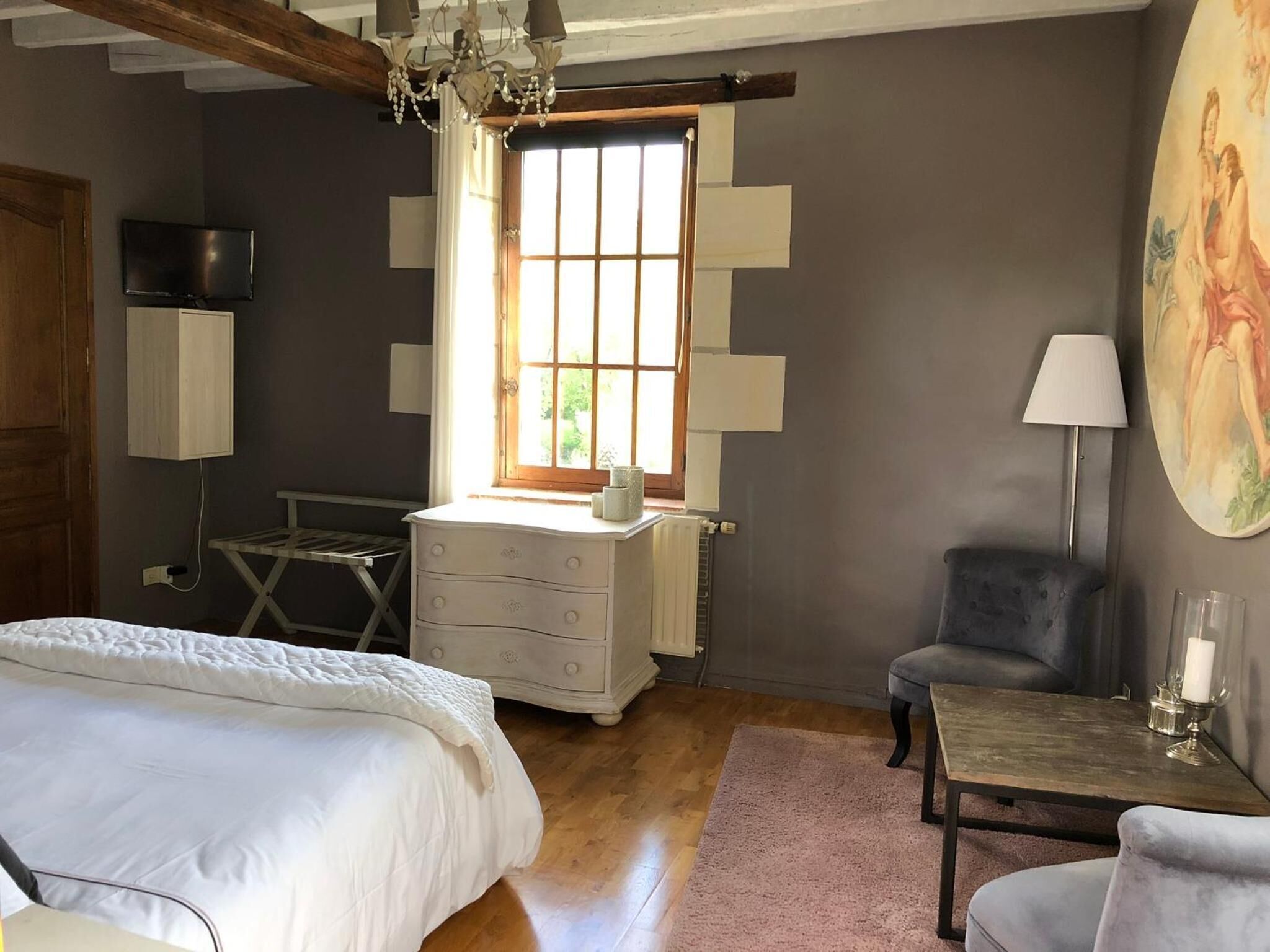 A bedroom with a bed, dresser, chair, and a table with a lamp.