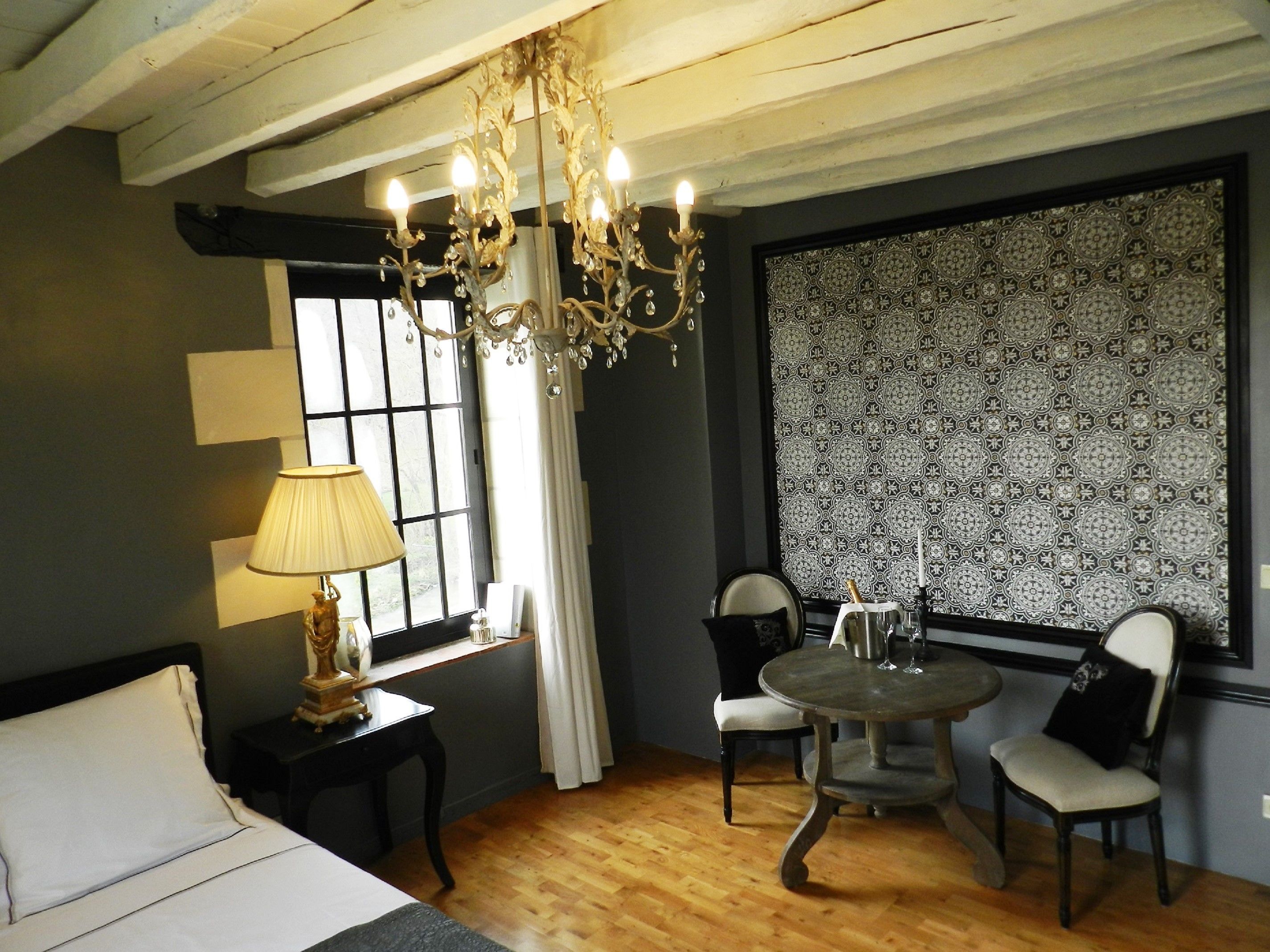 A room with a bed, a table with chairs, a chandelier, and a patterned wallpaper.