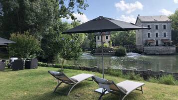 Un patio junto al río con dos sillones de relax y una gran sombrilla, con vistas a un edificio histórico y un río tranquilo.