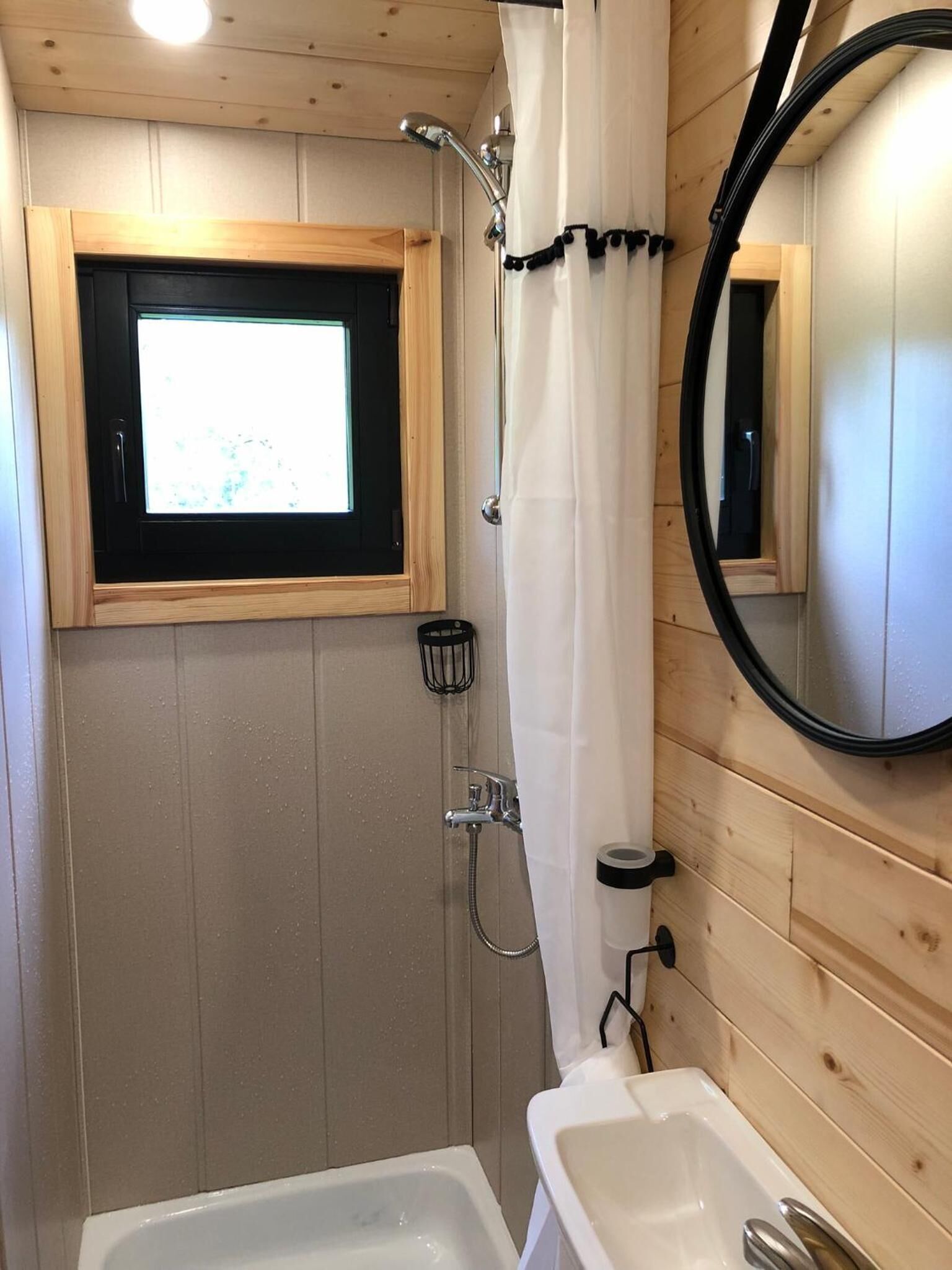 A compact bathroom with a shower, a small window, a mirror, and a sink.