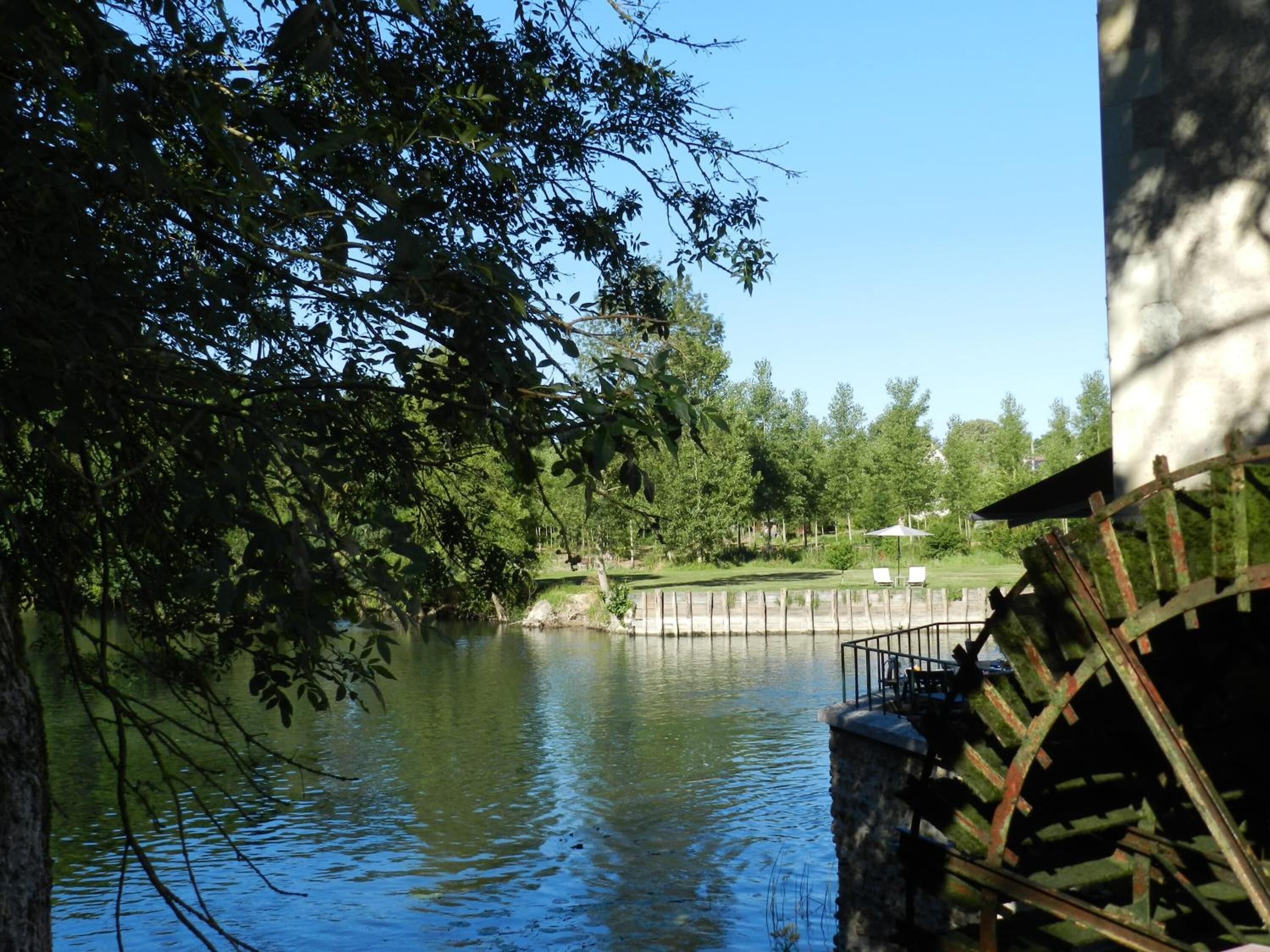 Una vista tranquila a la orilla del río, con una estructura de madera rústica y un muro de piedra.