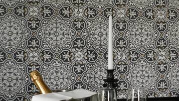 A table with a bottle of champagne, a candle, and two wine glasses against a patterned wallpaper background.