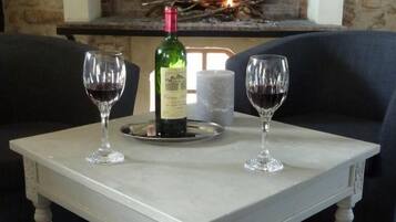 A marble table with two wine glasses and a bottle of wine in front of a fireplace.