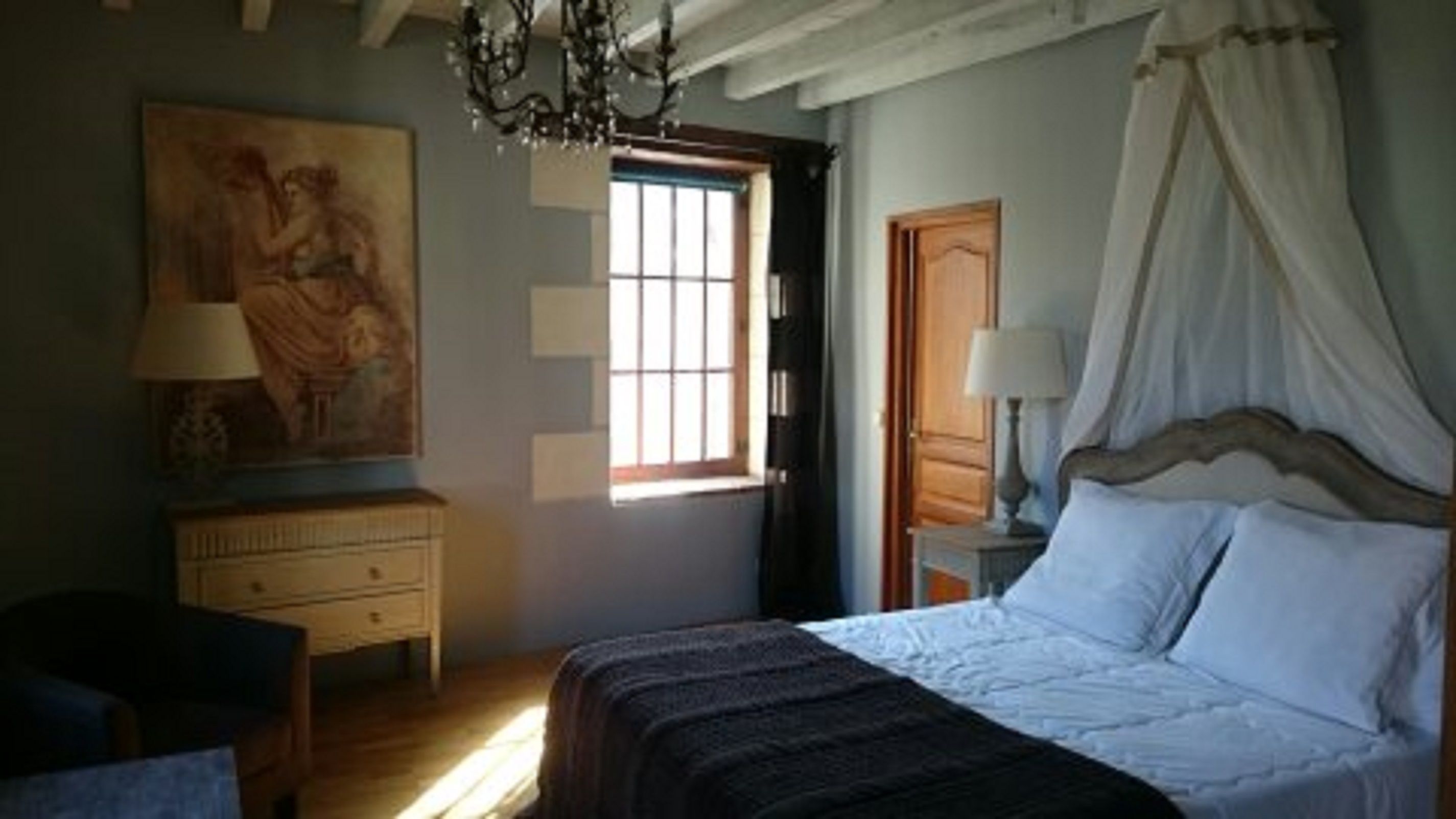 A bedroom with a bed, a nightstand, a dresser, a window with curtains, and a painting on the wall.