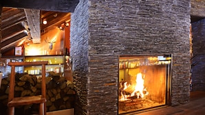 Une cheminée en pierre avec un feu de bois, une chaise en bois et une pile de bois de chauffage.