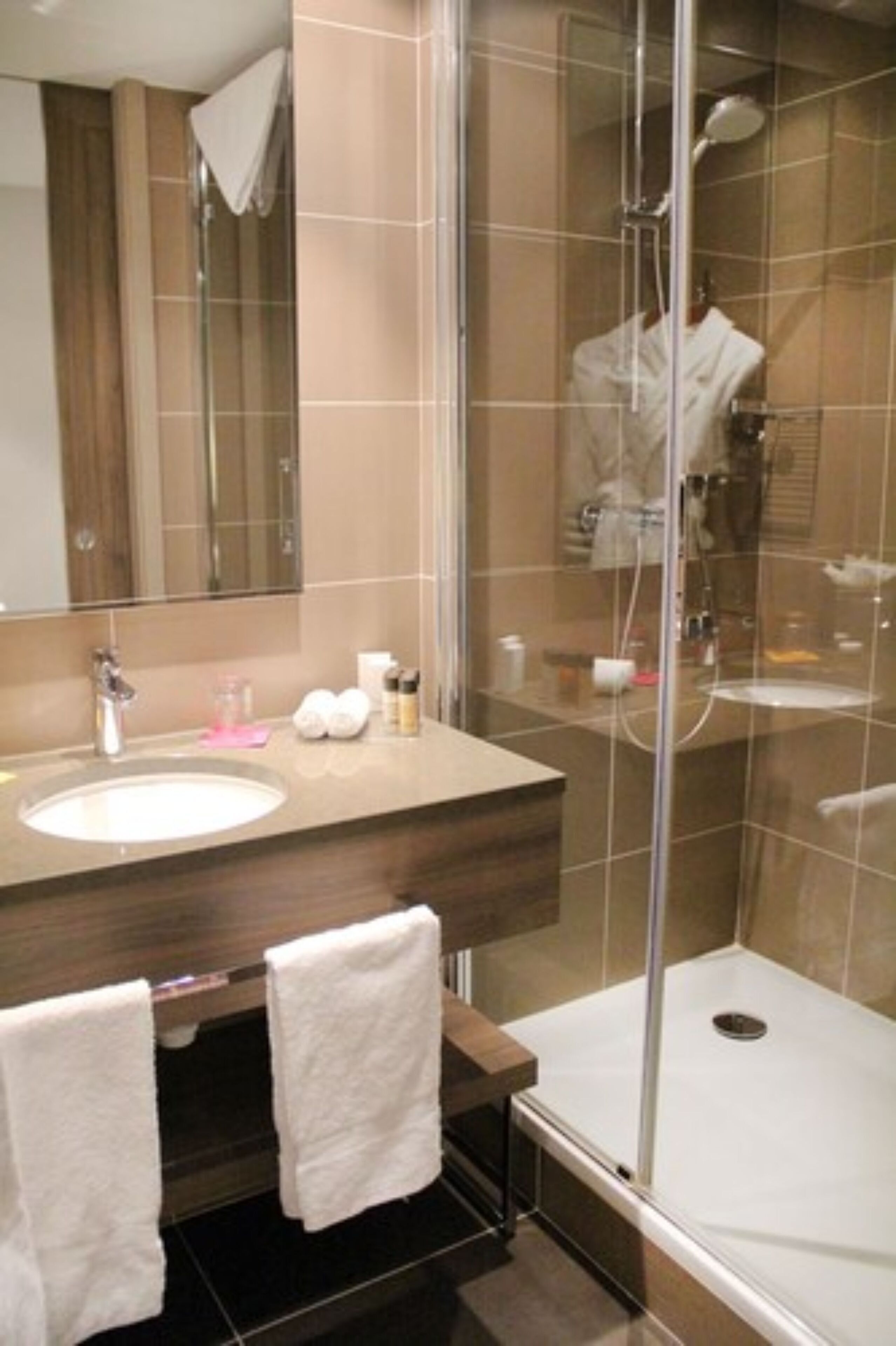 Un baño moderno con ducha envuelta en vidrio, tocador de madera y un espejo grande.